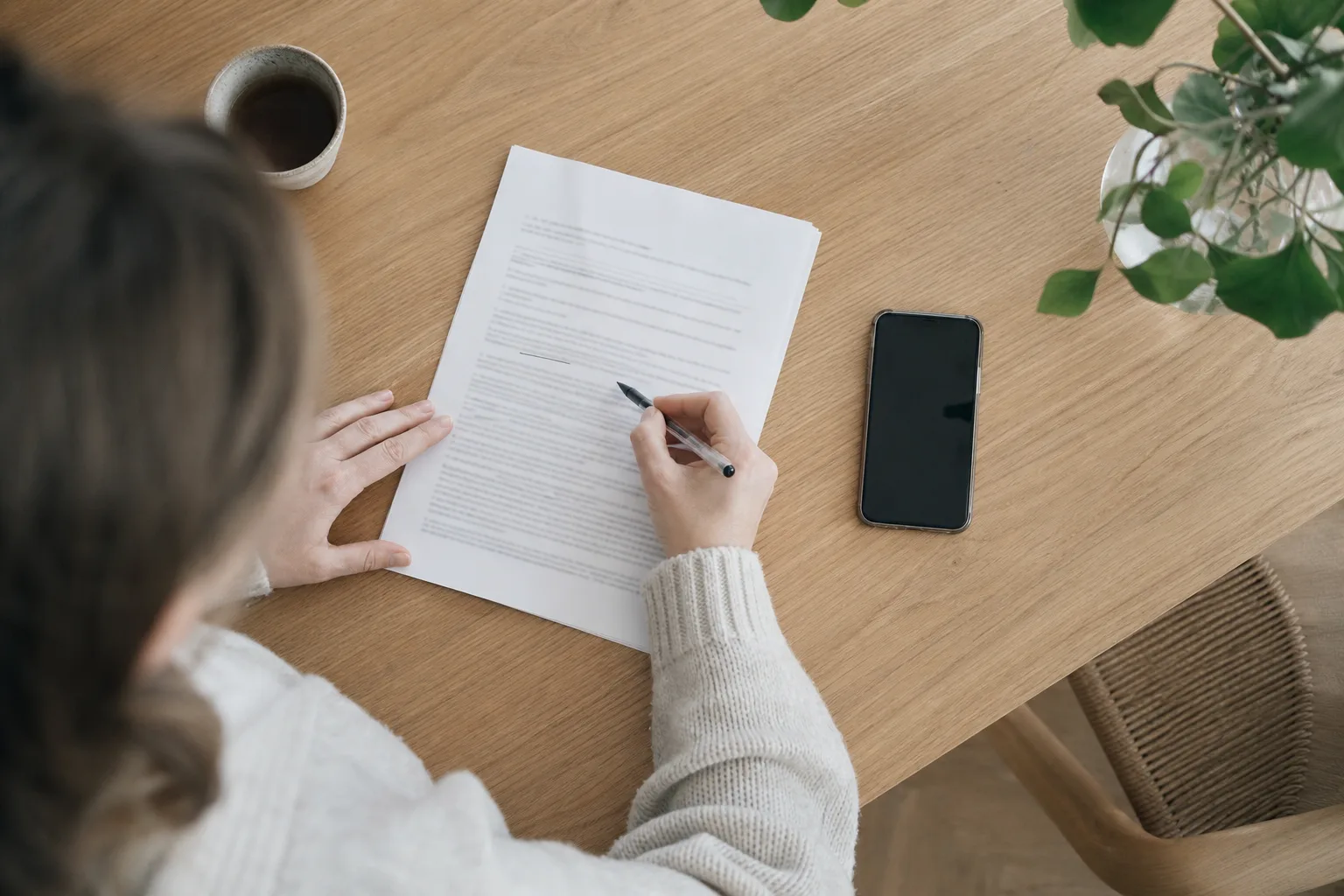 Närbild på ett mobilavtal och en mobil på ett bord där någon läser igenom villkoren för bindningstid innan byte