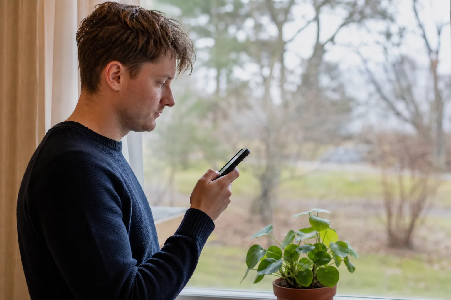 Person kollar mobiltäckningen på telefonen vid ett fönster i ett svenskt hem