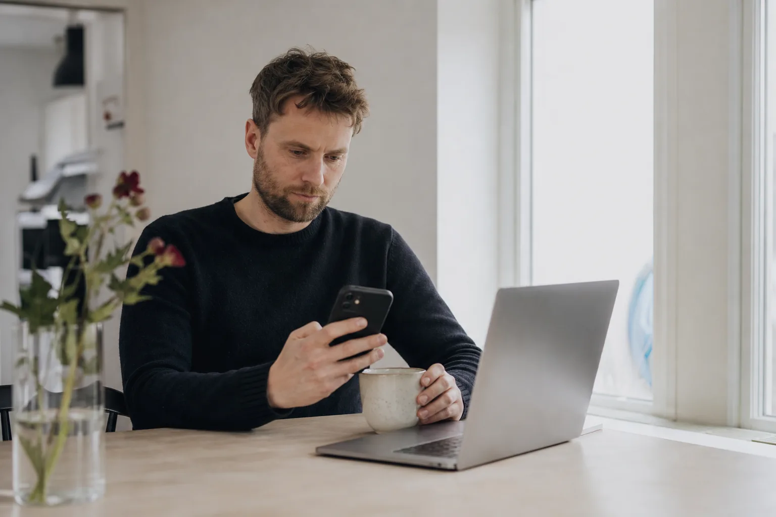 Person jämför mobilabonnemang i mobilen vid köksbordet inför ett byte till Comviq